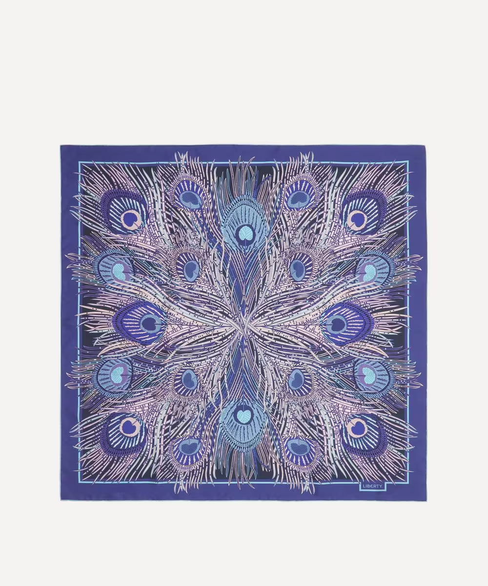 A square silk scarf featuring a symmetrical peacock feather pattern in shades of blue, purple, and white, bordered by a solid purple edge, displayed flat against a light gray background.