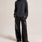 Woman wearing a dark gray sweater and black pants on a plain background