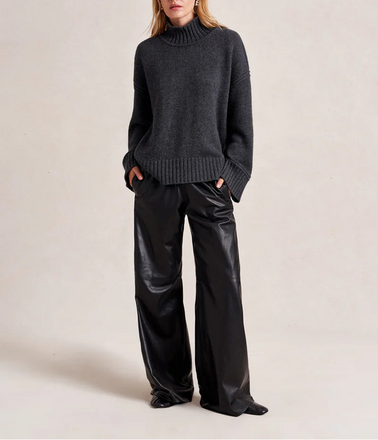 Woman wearing a dark gray sweater and black pants on a plain background
