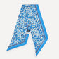 A blue silk scarf with a white floral print and a solid blue border, laid flat on a light gray background. A small black brand tag reading 'BONSAI' is visible near the center.