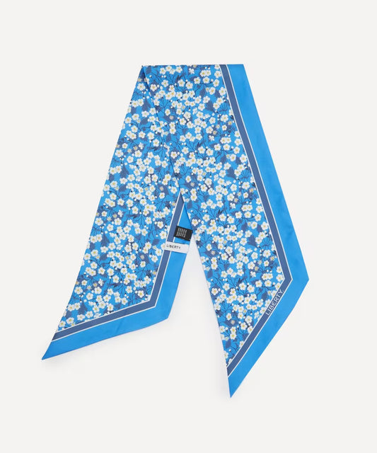 A blue silk scarf with a white floral print and a solid blue border, laid flat on a light gray background. A small black brand tag reading 'BONSAI' is visible near the center.